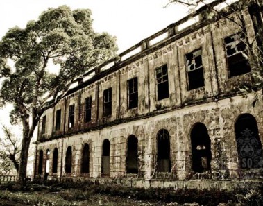 The decrepit stone facade of the Diplomat Hotel . There are two levels with large arched window frames. The windows appear to be long gone.