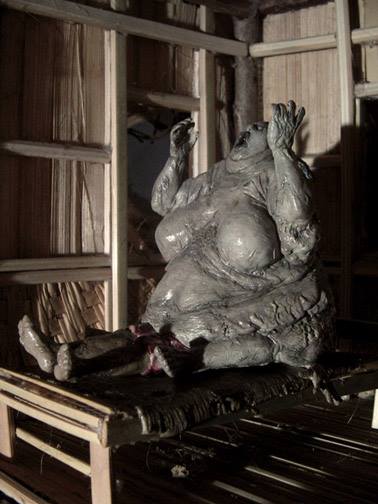 Sculpture of an morbidly obese female spirit smothering a sleeping male by sitting on him. 