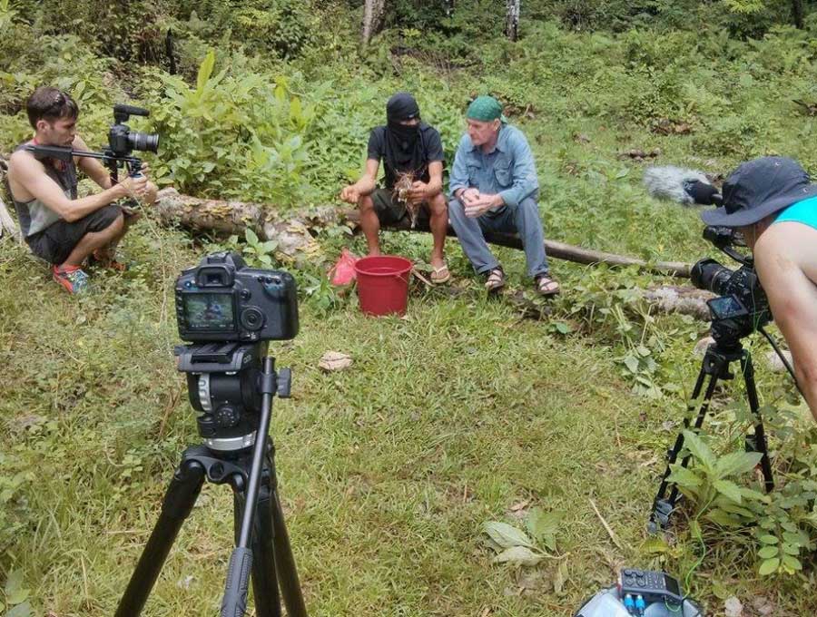 Matt and his crew filming "Search For The Aswang" Will sits with the Mababarang on a log with two SLR cameras pointed at them.