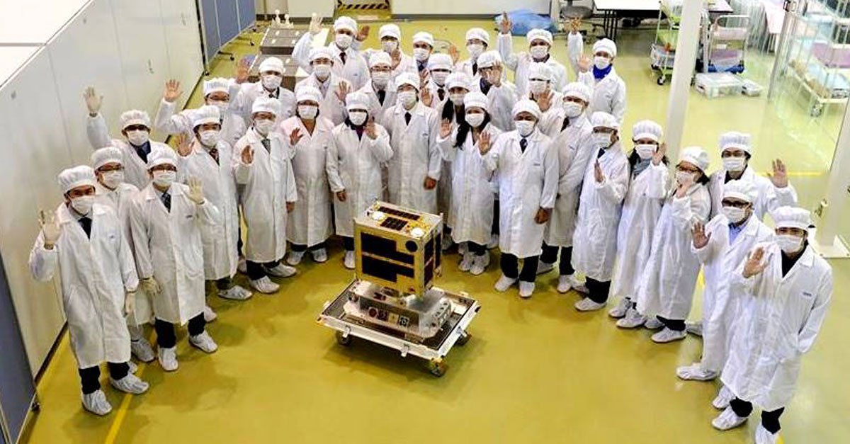 The Diwata-1 team stand around the satellite dressed in their white laboratory work wear. 