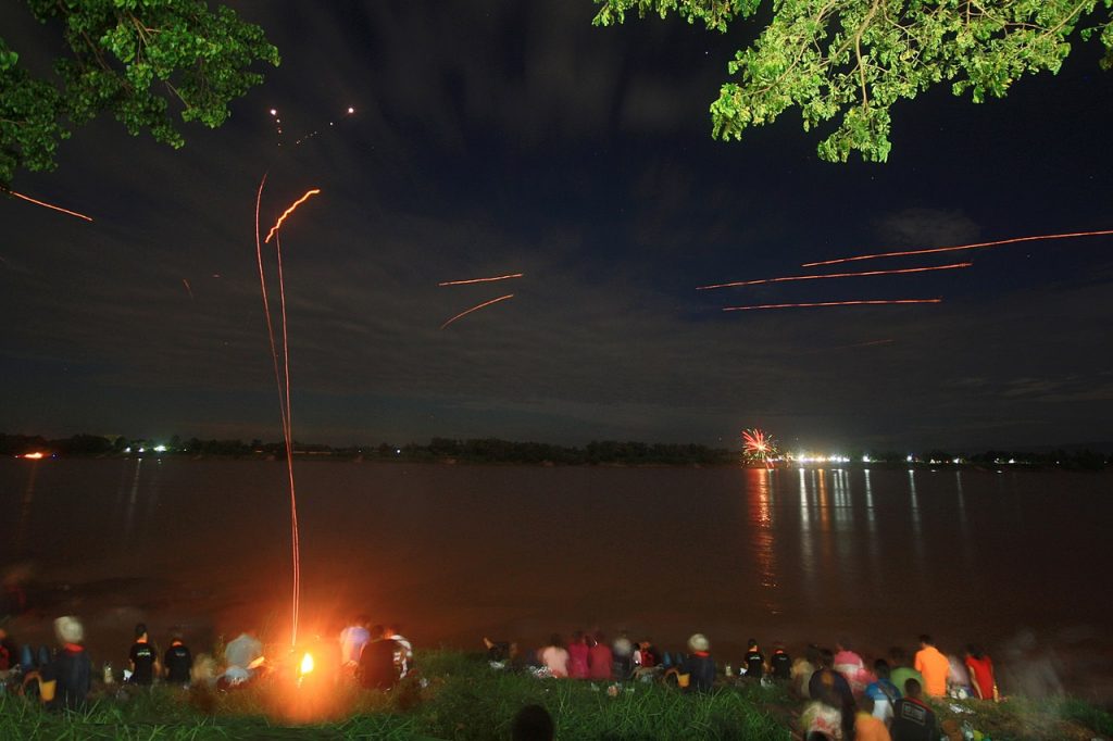The tracks of two Naga fireballs (at left) rising vertically into the sky before petering out near the top of the photo. The other tracks are of sky lanterns or fireworks.