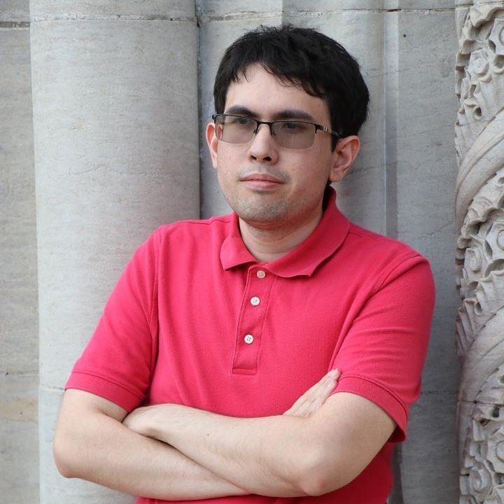 A young Filipino American man stands with arms crossed against a cement wall. He wears a salmon coloured polo shirt. 