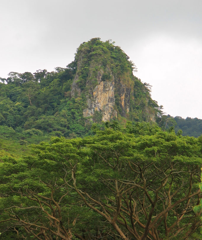 A large white rock, with some green growth is seen jutting from the mountainside of Arayat.