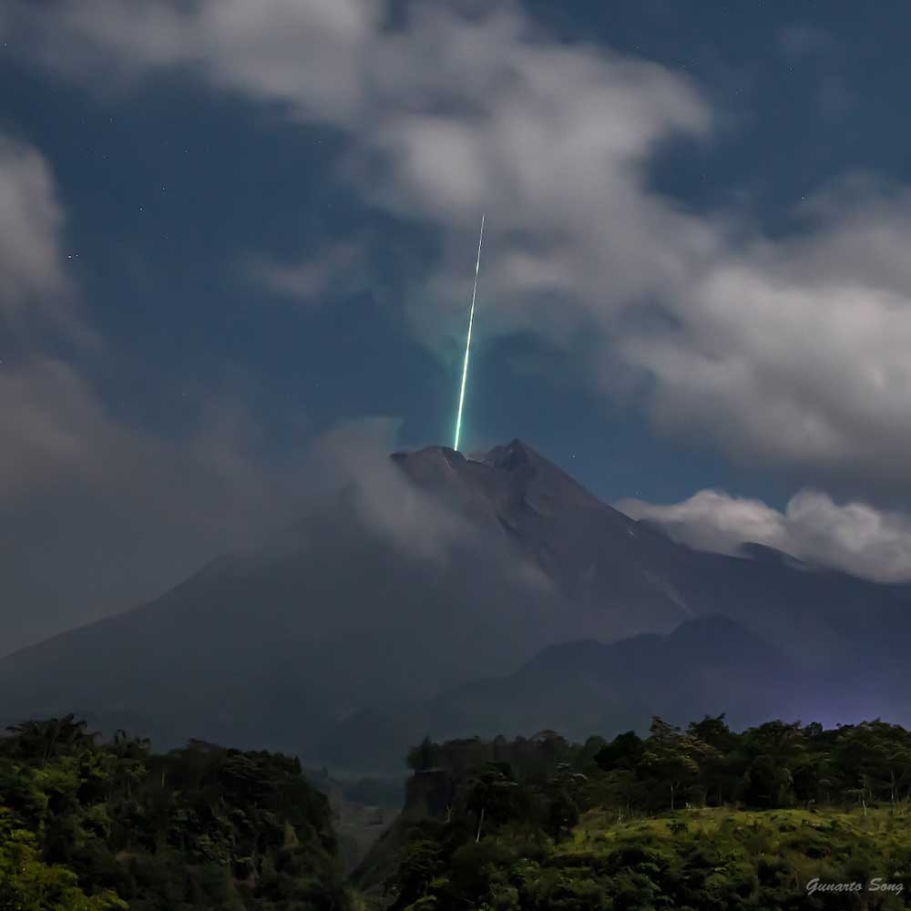A shooting star trails into the peak of a dormant tropical volcano.