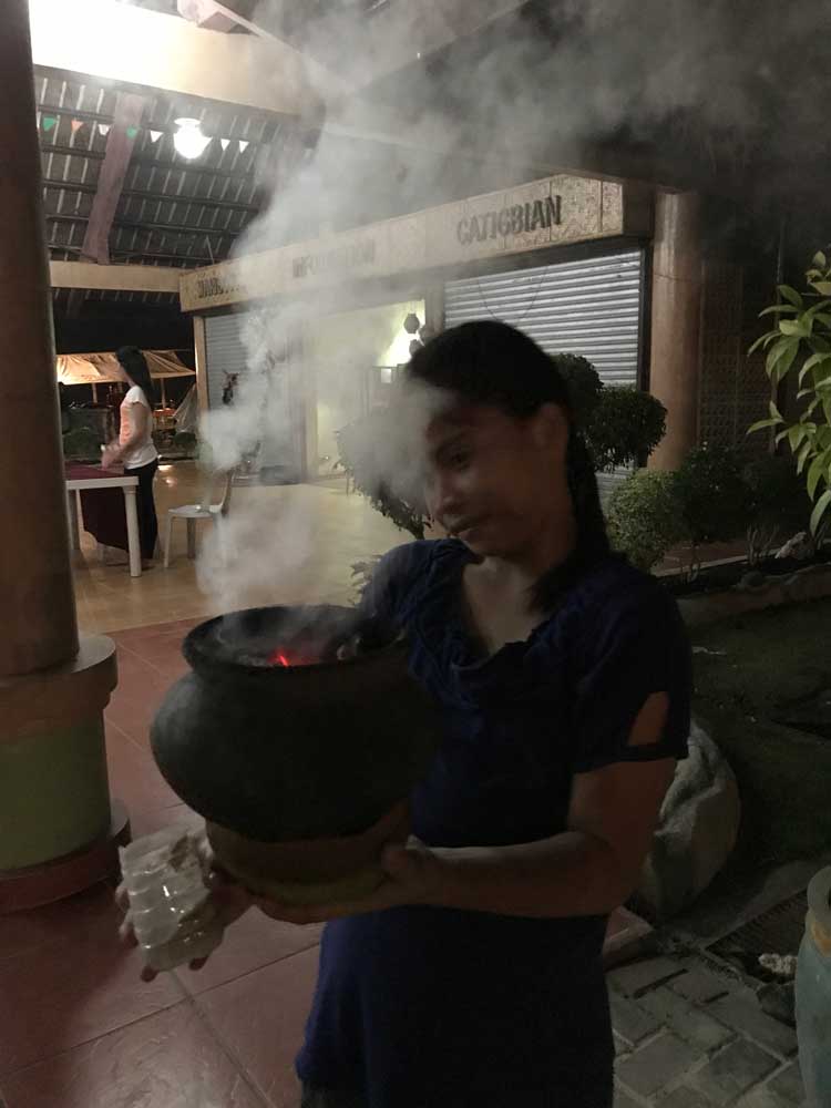 A girl stands with a pot, burning incense. 