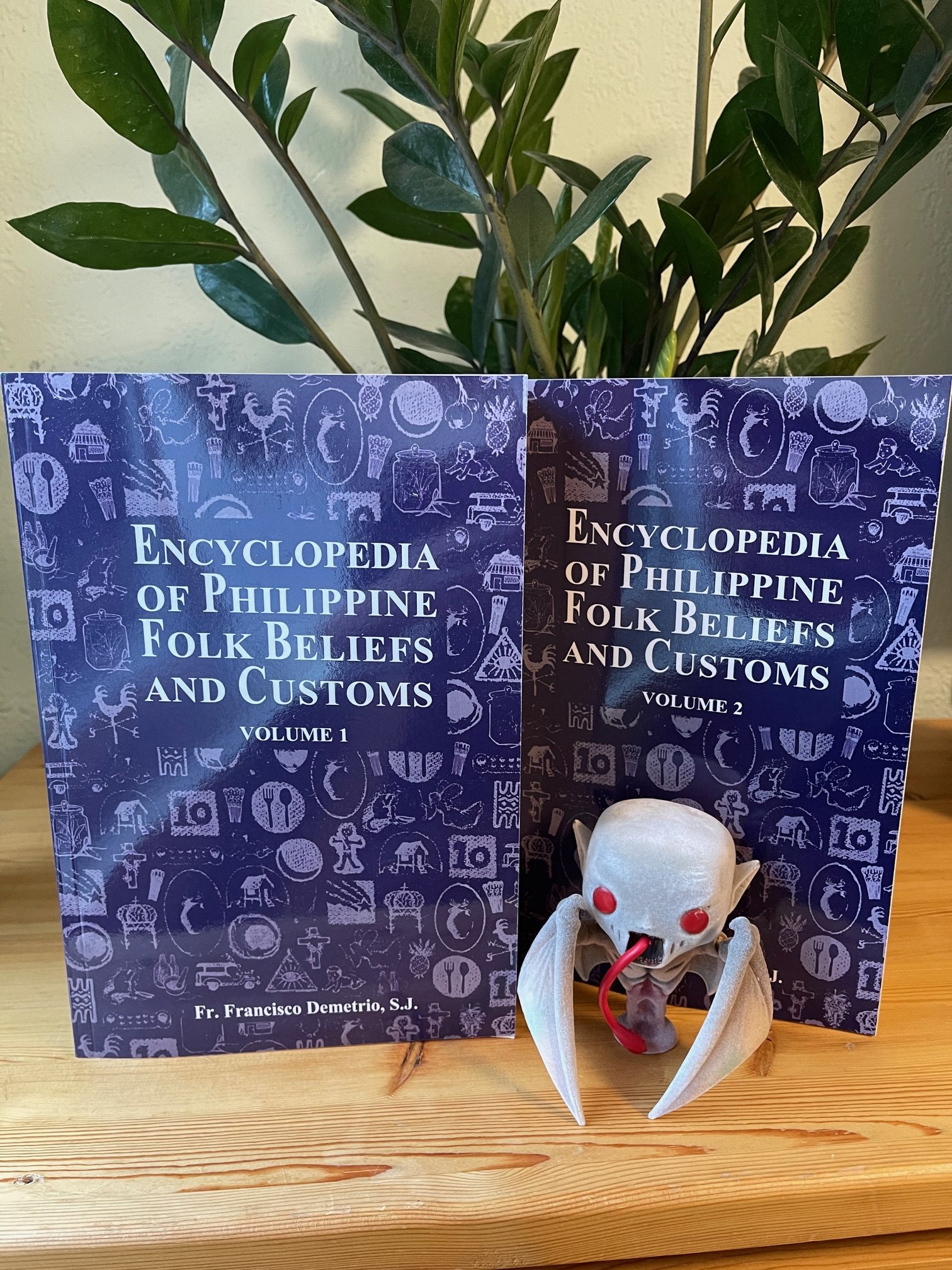 Photo of the Encyclopedia of Philippine Folk Beliefs and Customs book covers displayed on a pine shelf in front of a small folkloric figurine.